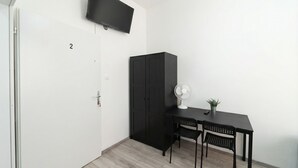 A room with a door labeled '2', a black cabinet, a desk with two chairs, a wall-mounted TV, a standing fan, and a small potted plant. - Quick Access to Vienna Center - Simple Private Rooms with WIFI (Vienna)