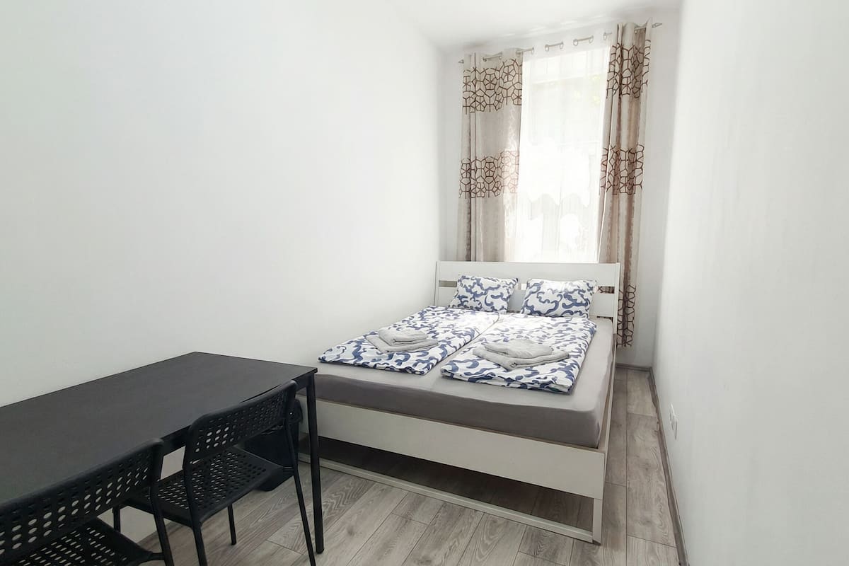 Una habitación pequeña con cama individual, un escritorio, una silla, una ventana con cortinas y suelo de madera.