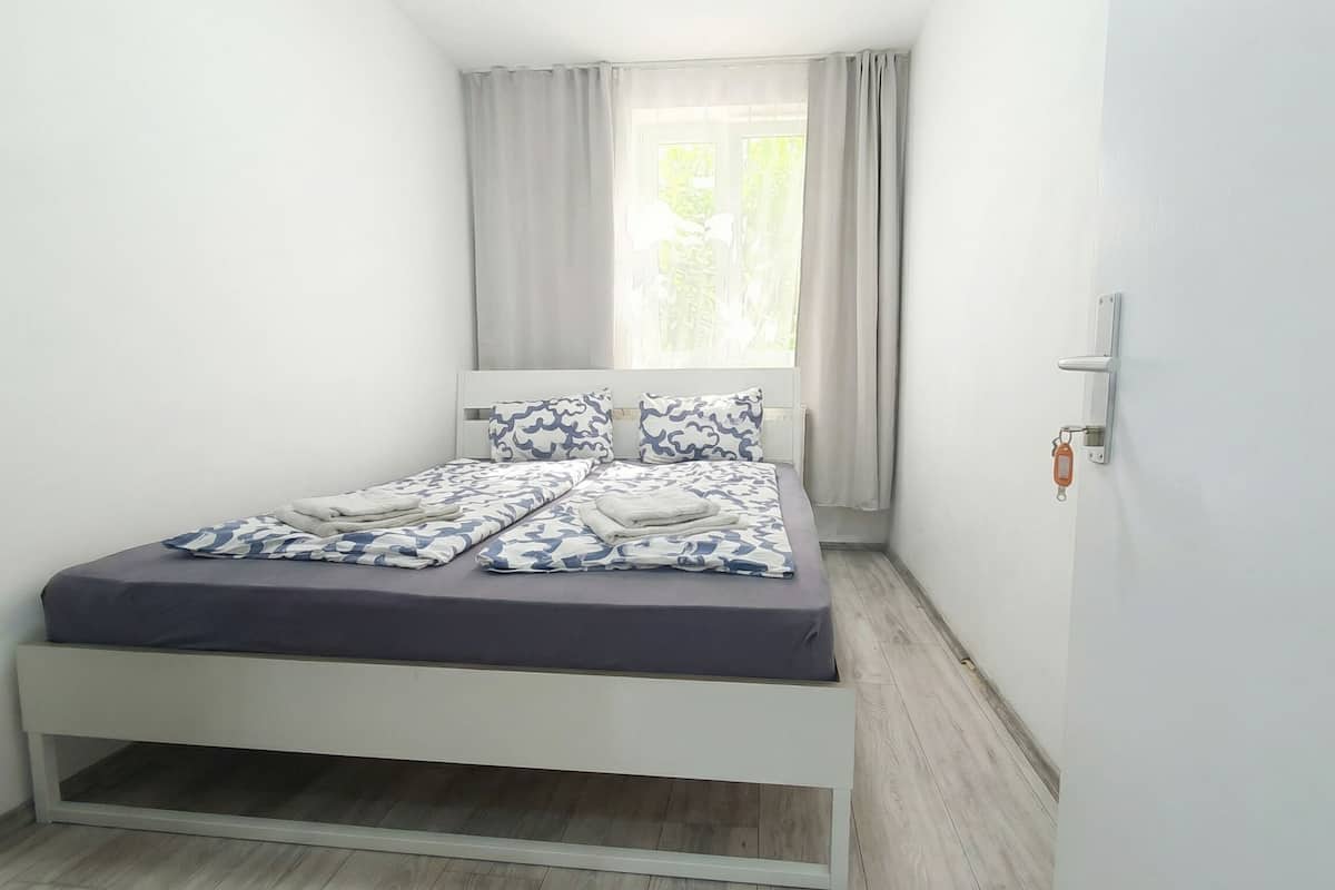 Un dormitorio pequeño y moderno con cama, una ventana con cortinas y una puerta con llavero.