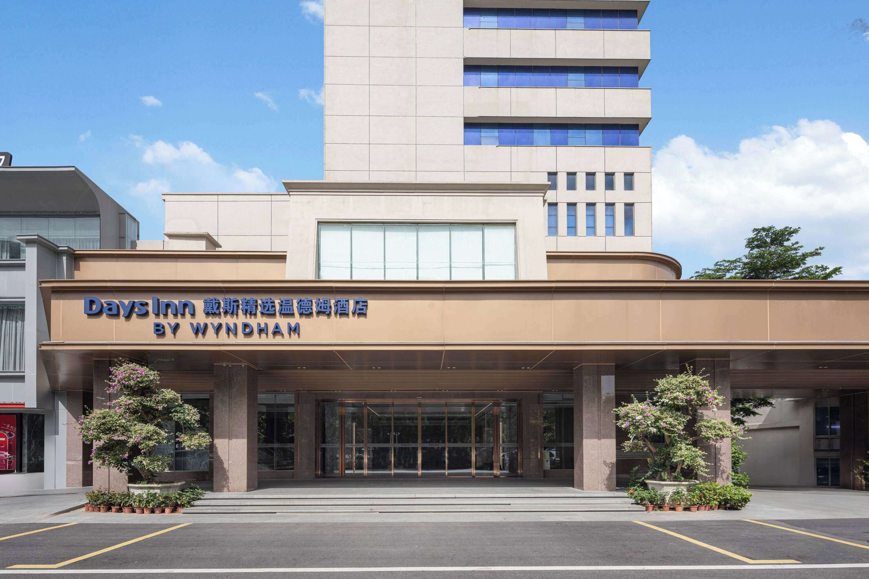 A Days Inn by Wyndham hotel entrance with a modern design, large glass doors, and potted plants.