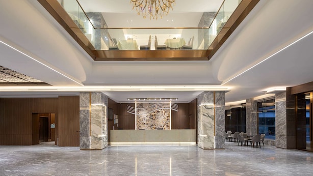 Un hall d’entrée spacieux, doté d’un comptoir de réception en marbre, d’un lustre et d’une balustrade en verre donnant sur un niveau inférieur.