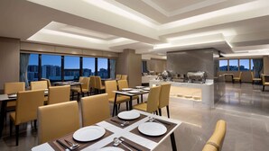 Un espace de restauration moderne avec des tables disposées pour accueillir quatre personnes, un bar et une vue sur le paysage urbain.