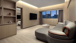 Un salon moderne avec un canapé, un téléviseur à écran plat et une vue sur la ville grâce à de grandes fenêtres.