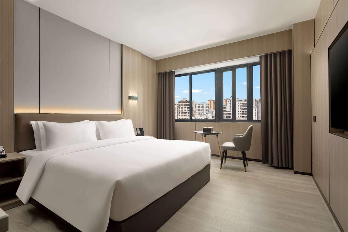 A modern hotel room with a large bed, a desk, a chair, and a TV.