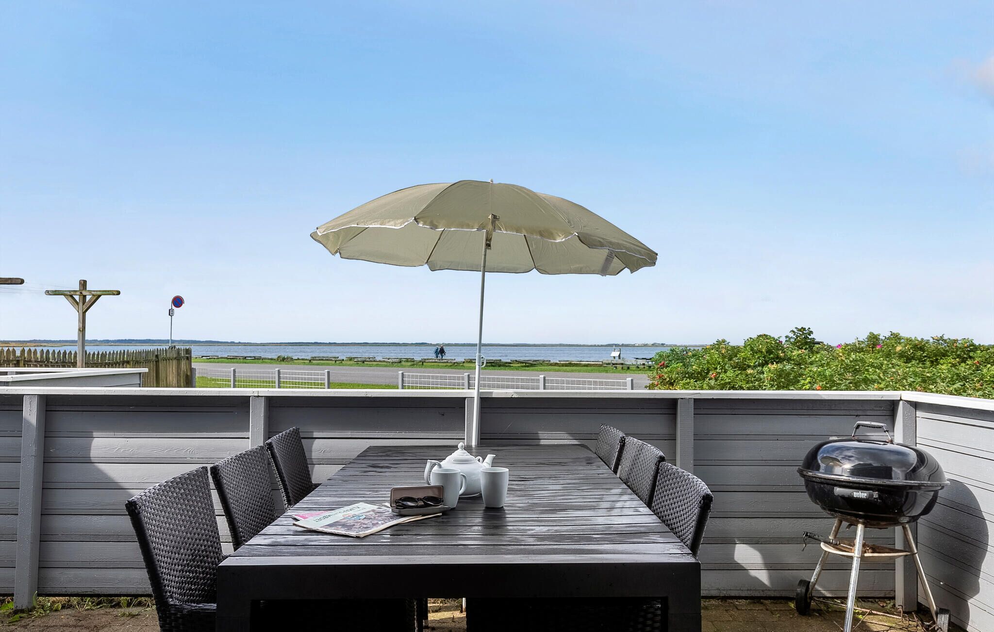 Une terrasse avec une table, des chaises, un parasol et un barbecue.