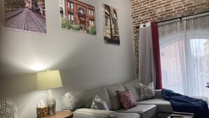 Een woonkamer met een bank, een bijzettafeltje met een lamp en een raam met gordijnen.