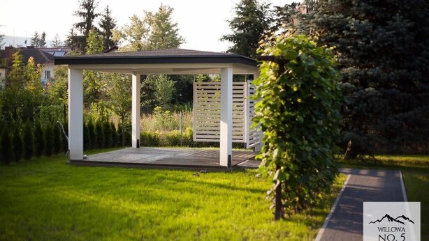 Een prieeltje in een verzorgde tuin, met een geplaveid pad er naartoe.