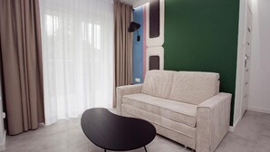 Een moderne kamer met een beige bank, een zwarte stoel en een groene accentmuur.