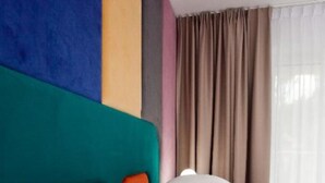 Een hotelkamer met een kleurrijk hoofdeinde, een bed met witte lakens en een raam met beige gordijnen.