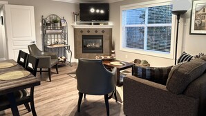 A living room with a fireplace, television, dining area, and a large window. - Charming Mill Bay 2 Br Suite (Mill Bay)