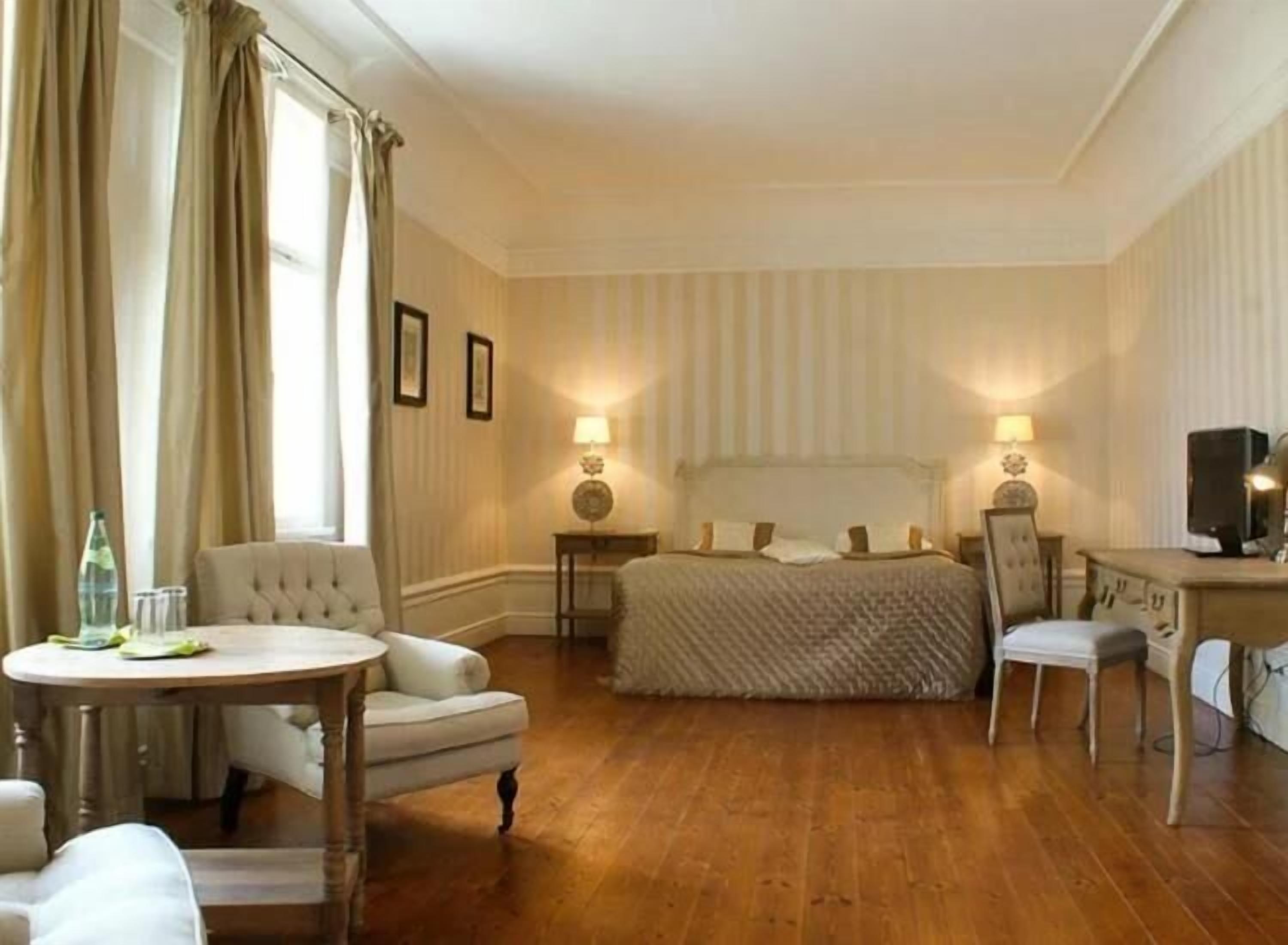 Una habitación de hotel con una cama grande, dos mesitas de noche con lámparas, una mesa redonda con una silla y un televisor sobre un escritorio.