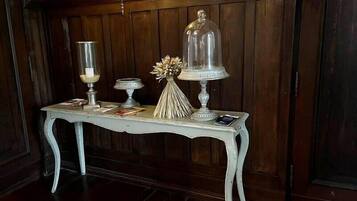 A white table with a glass dome centerpiece, a candle holder, and a decorative vase against a wooden wall.