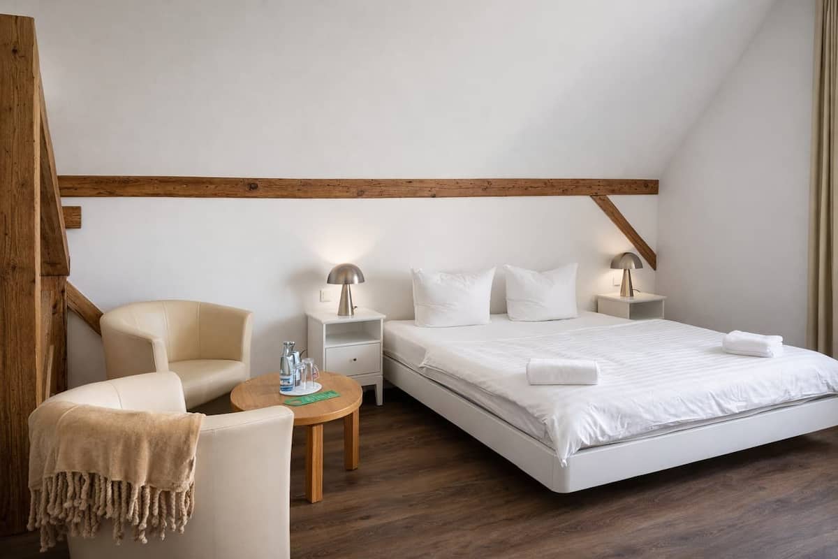 Ein Hotelzimmer mit einem großen Bett, einem Sessel, einem kleinen Tisch und zwei Nachttischen mit Lampen.