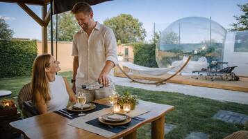 An outdoor dining area with a table set for two, a hammock, and a transparent dome structure in the background.