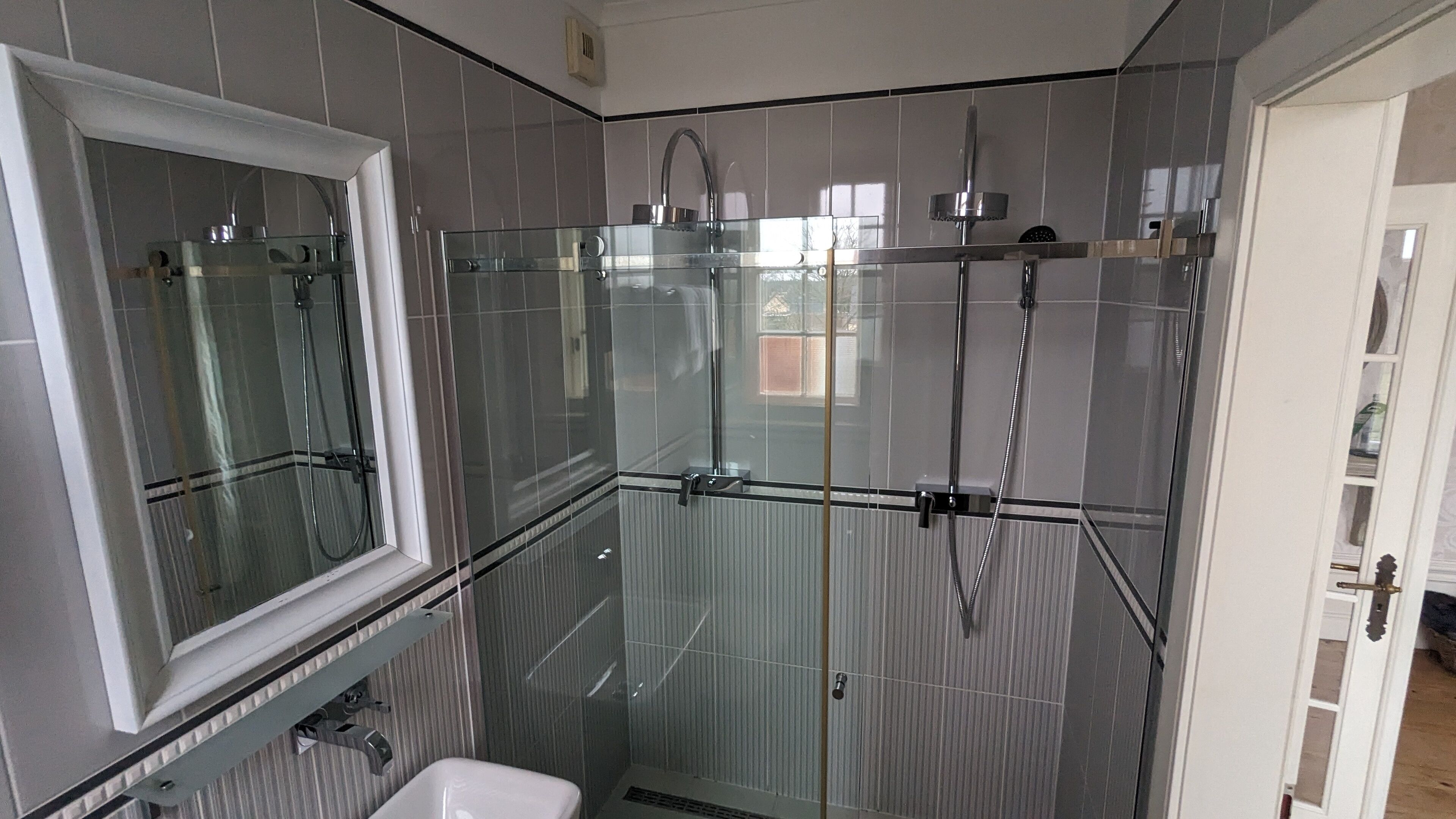 A modern bathroom with a glass shower enclosure, a window, and a white sink.