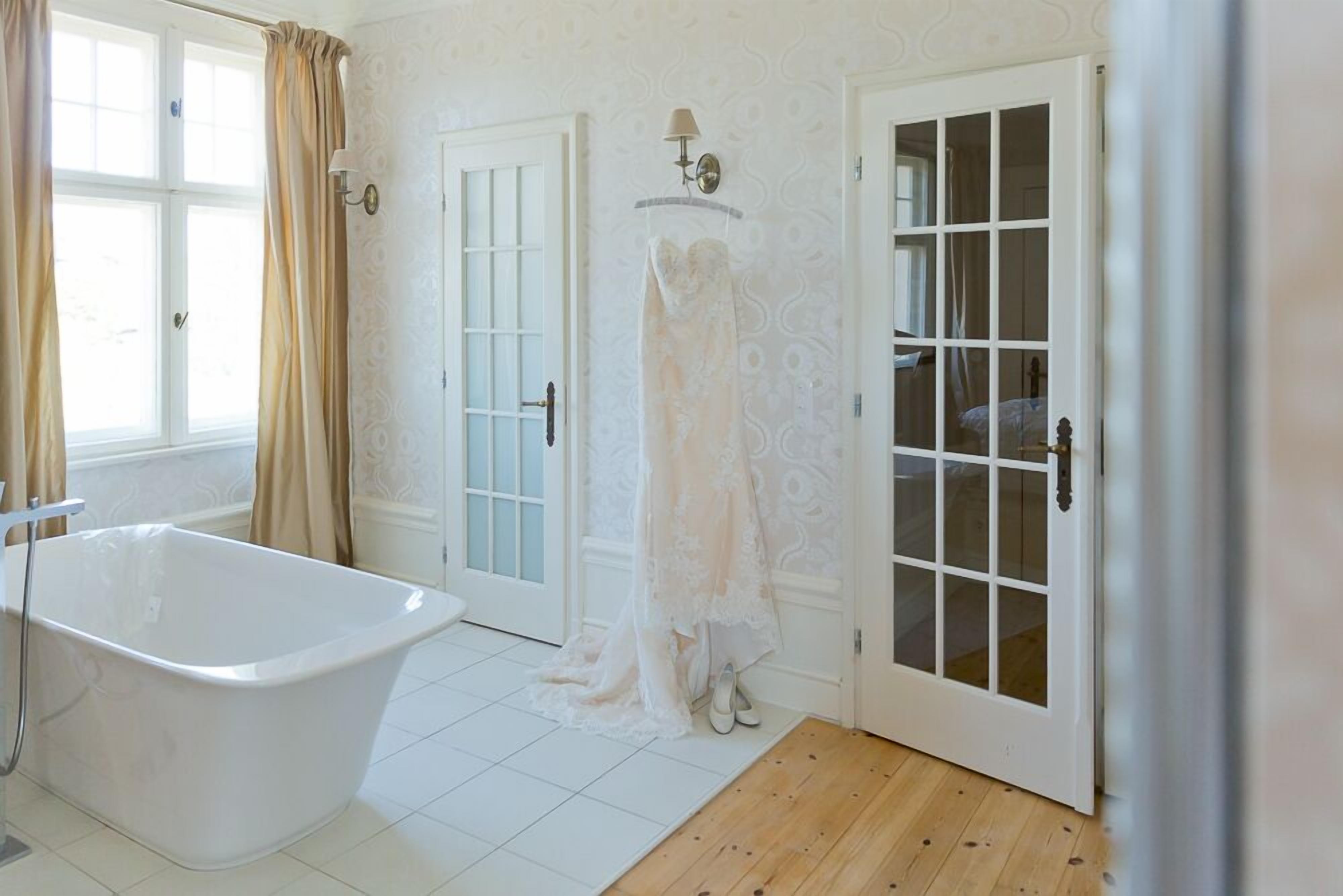 A bathroom with a freestanding bathtub, a door with glass panels, and a white patterned wall.