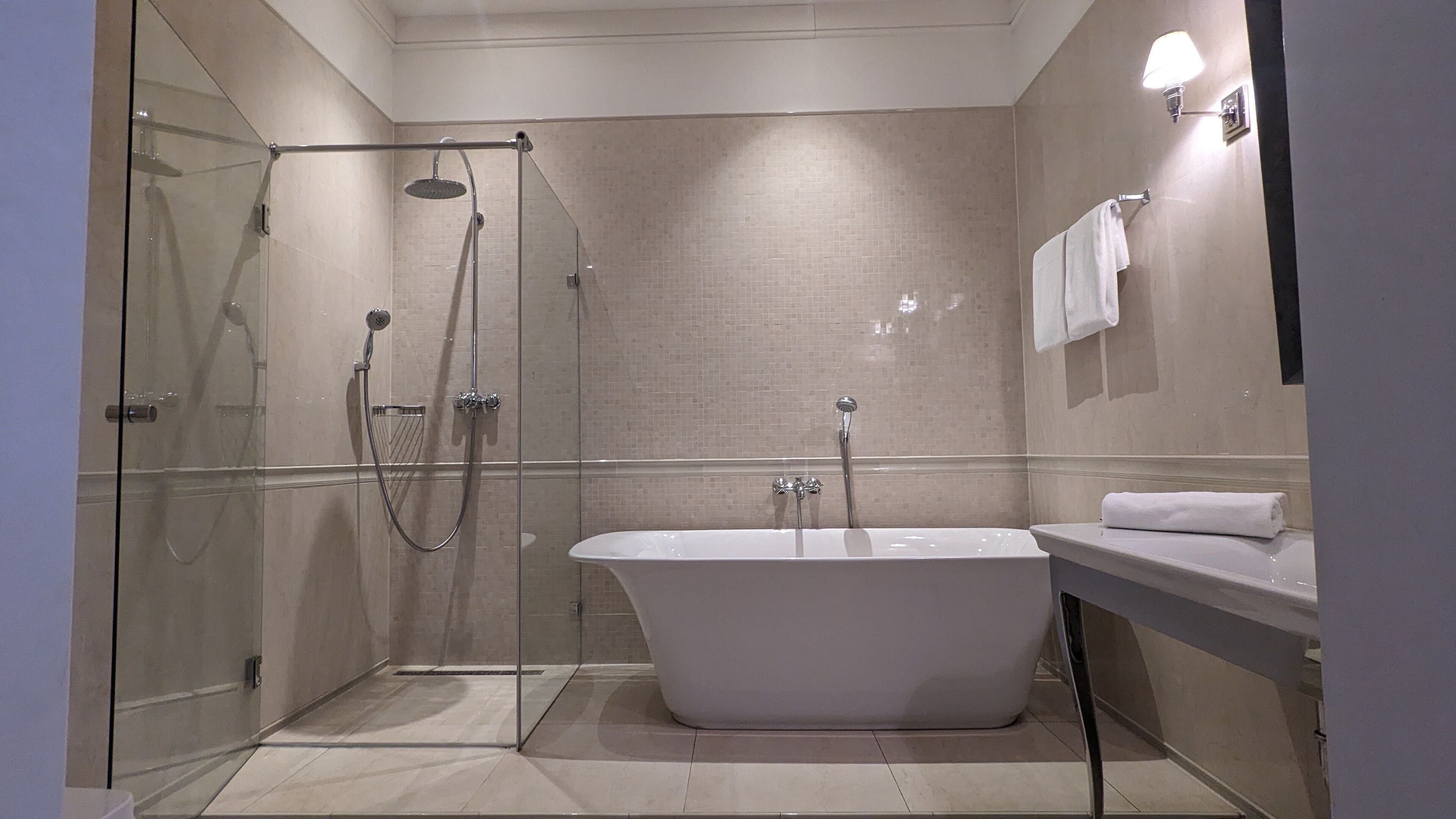 A modern bathroom with a glass-enclosed shower, a freestanding bathtub, and a vanity with a mirror and towel rack.
