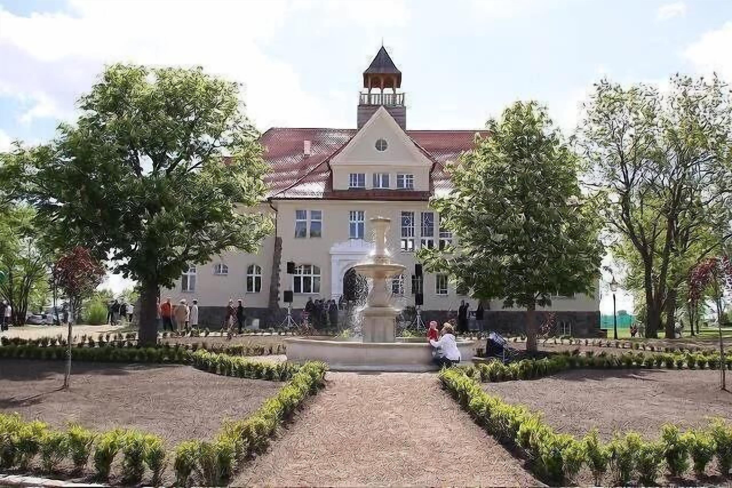 A large building with a central fountain, surrounded by well-maintained gardens and pathways.