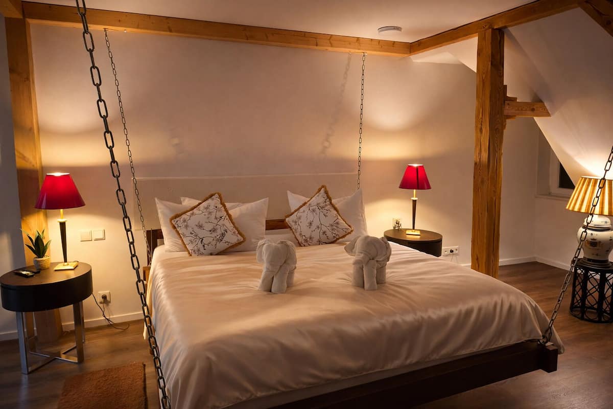 Ein Schlafzimmer mit einem Hängebett, zwei Nachttischen mit Lampen sowie einer Holzbalkendecke.