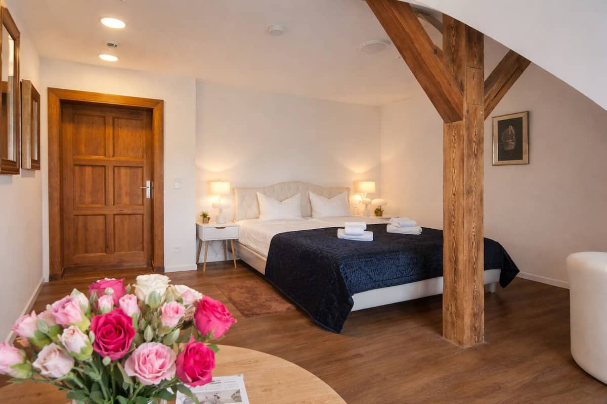 Ein Hotelzimmer mit Bett, Nachttischen, einem Holzbalken an der Decke und einer Holztür.