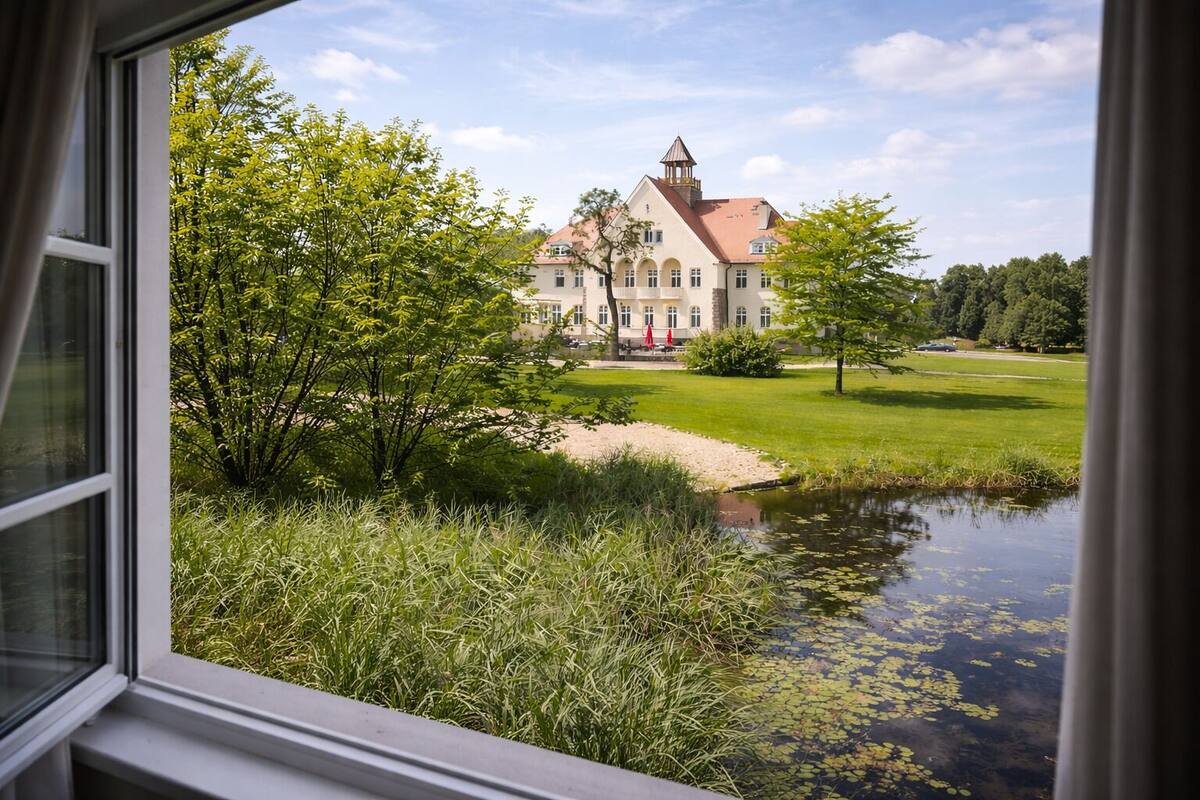 Blick auf ein Gebäude mit einem Turm, umgeben von Grünflächen und einem Teich.