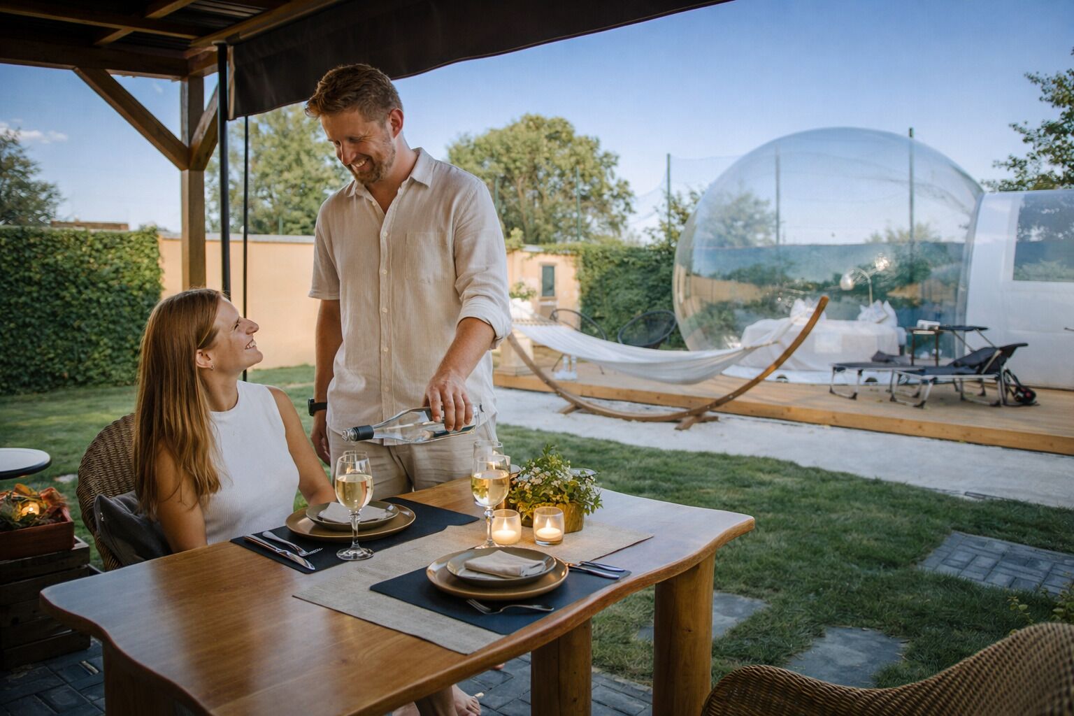 An outdoor dining area with a table set for two, a hammock, and a transparent dome structure in the background.
