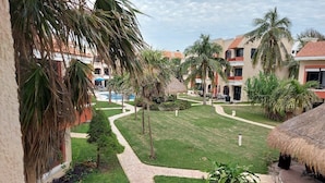 A resort courtyard with palm trees, a swimming pool, and a thatched-roof structure. - Casa Playasol (Puerto Morelos)