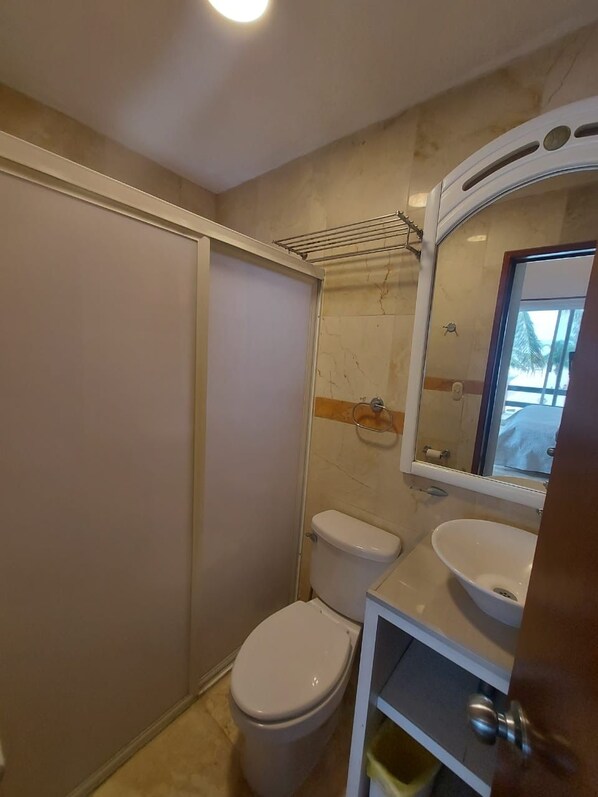 A compact bathroom with a toilet, sink, and a mirror. - Casa Playasol (Puerto Morelos)