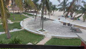 A courtyard with a circular seating area, palm trees, and a beach view. - Casa Playasol (Puerto Morelos)