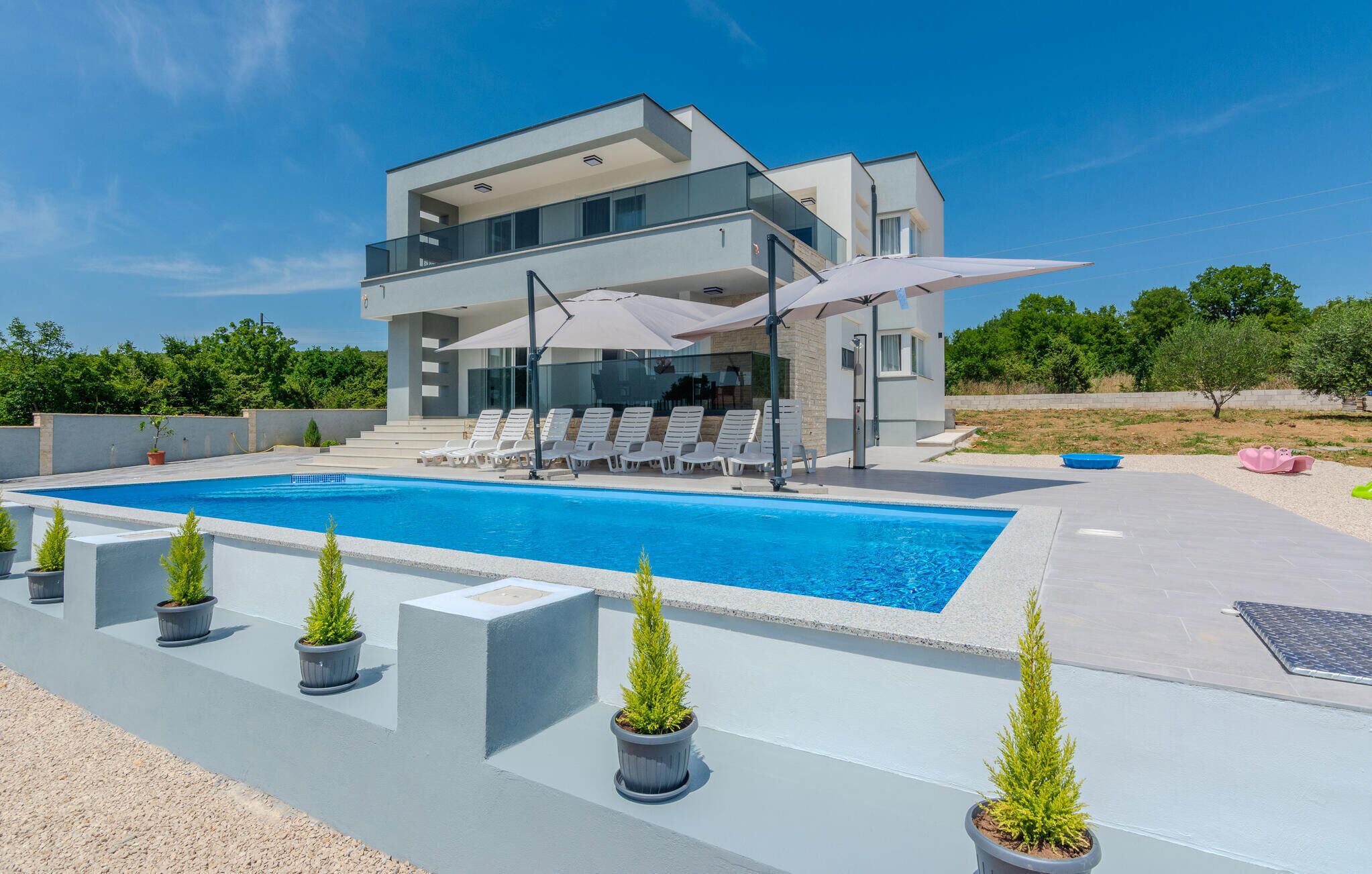 Una casa moderna de dos pisos con piscina, sillas de tomar el sol y plantas en macetas.