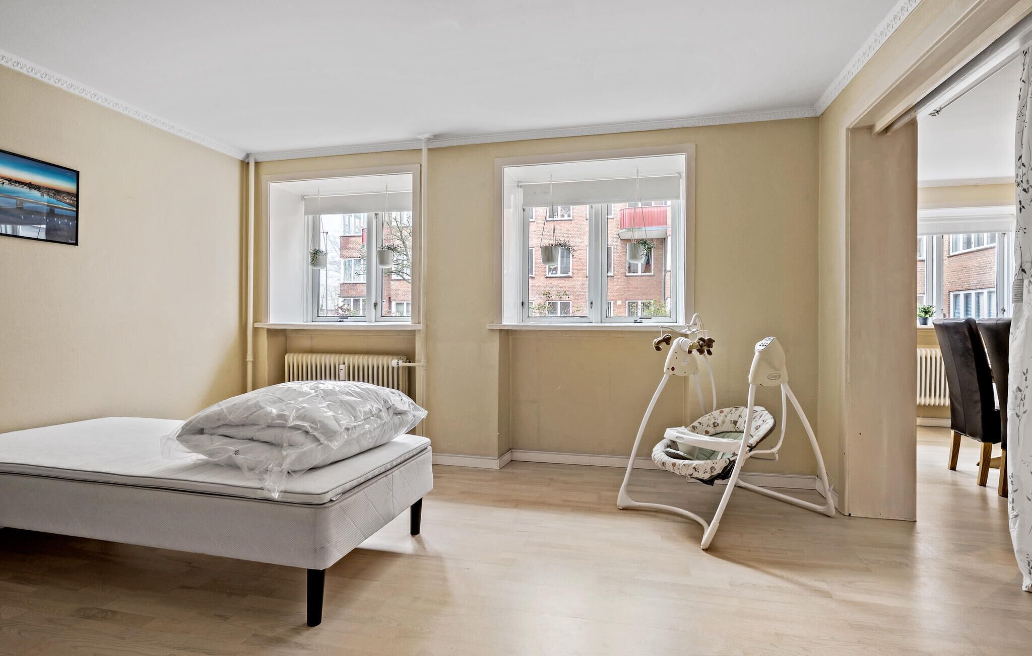 A bedroom with a bed, a window, a radiator, and a baby rocker.