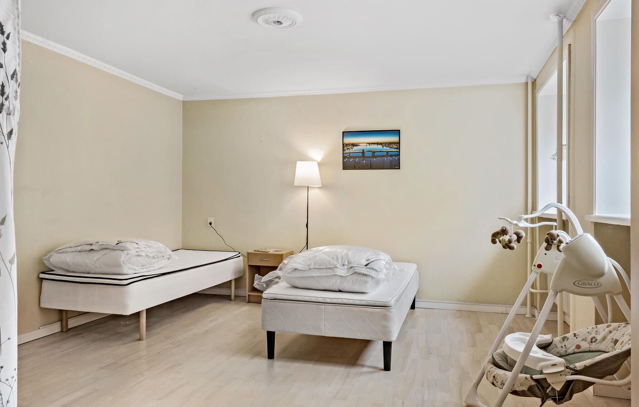Une chambre d’enfant avec un lit, un berceau, une table de chevet, une lampe et un tableau accroché au mur.