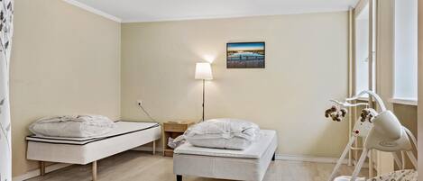 Habitación infantil con cama, cuna, mesita de noche, lámpara y un cuadro en la pared.