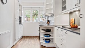 Une cuisine compacte avec des meubles blancs, une fenêtre et une étagère intégrée où sont rangées des casseroles.