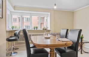 Un espace repas comprenant une table ronde en bois, des chaises en cuir noir et une vue sur un bâtiment en briques, visible à travers de grandes fenêtres.