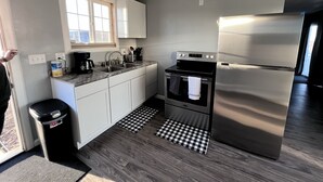A modern kitchen with white cabinets, a stainless steel refrigerator, a built-in oven, and a coffee maker.