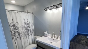 A bathroom with a shower curtain, toilet, sink, and wooden cabinet.