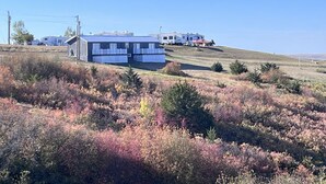 A mobile home with a blue roof and white trim, situated on a grassy hill with autumn-colored vegetation.