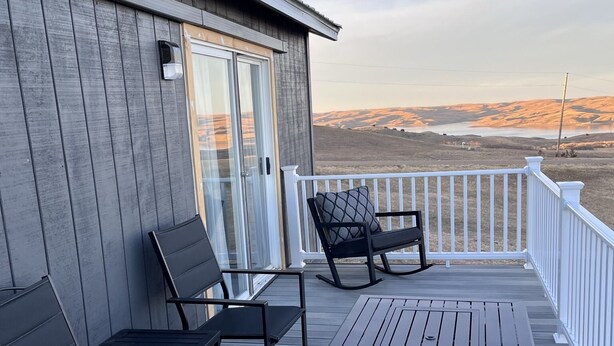 A deck with a table and chairs, a sliding glass door, and a view of a landscape.
