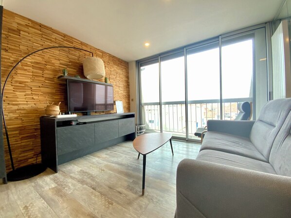 Una sala de estar moderna con un televisor de pantalla plana, un sofá, una mesa de centro y un ventanal con vistas.