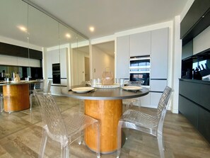 A modern kitchen with a round dining table, clear chairs, and built-in appliances.