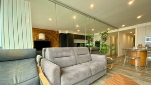 Una sala de estar moderna con un sofá gris, suelo de madera, una mesa de centro de madera y una zona de cocina al fondo.
