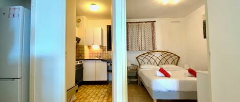 Una habitación de hotel pequeña con cama, mesita de noche y una kitchenette.
