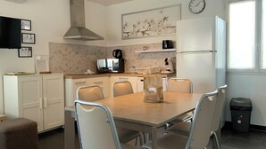 A modern kitchen with white cabinets, a dining table with chairs, a microwave, a coffee maker, and a clock on the wall.