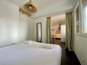A hotel room with a large bed, a wardrobe, a mirror, a kitchenette, and a view of the outside.