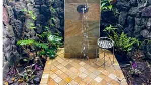 A rectangular stone water feature with a spout, surrounded by a stone wall and various plants. - Tropical Ocean View! Escape to the Rainforest getaway of your dreams! (Keaau)