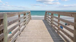A wooden boardwalk leading to a beach with clear skies and calm waters. - Gorgeous Beachfront Condo with Pool (Surf City)