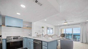 A modern kitchen with blue cabinets, a central island, and a view of the ocean through large windows. - Gorgeous Beachfront Condo with Pool (Surf City)