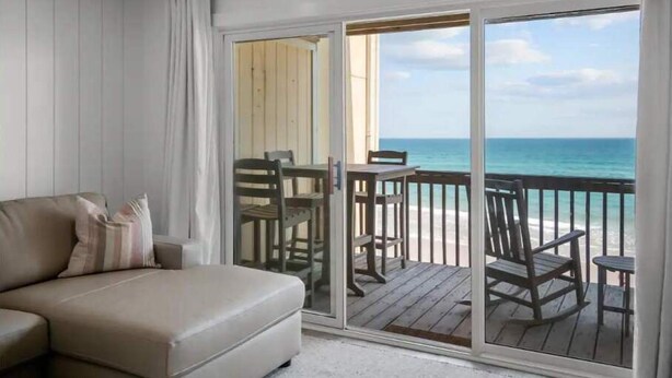 A balcony with a view of the ocean, a sofa, and a table with chairs. - Gorgeous Beachfront Condo with Pool (Surf City)