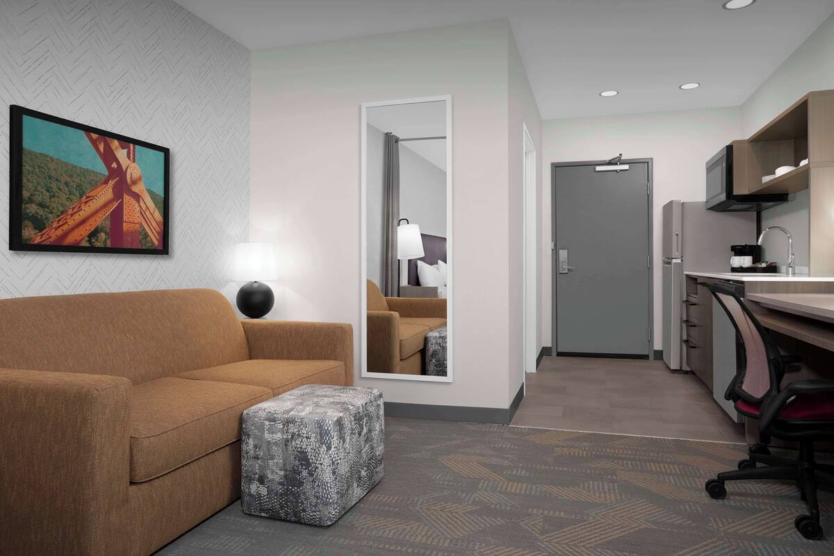A modern hotel room with a sofa, ottoman, and a large mirror.